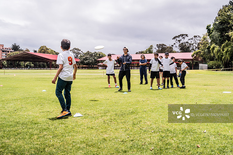教练在运动场上向学生教授飞盘基础知识图片素材