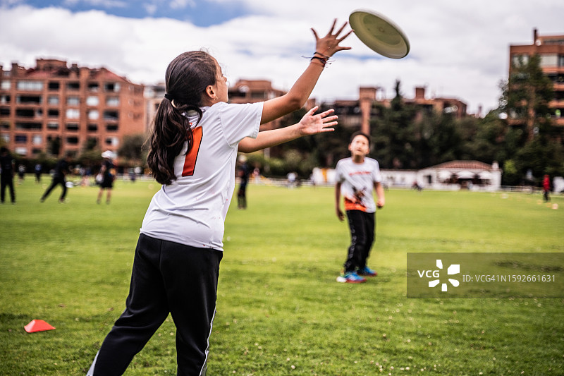 女孩在公园里和朋友们玩飞盘的背影图片素材