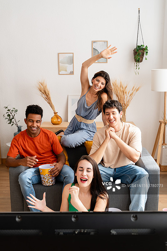朋友们在家里的客厅里一边吃着爆米花一边看电影庆祝图片素材