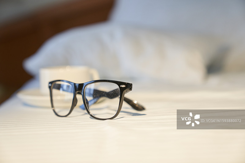 酒店房间的床上放着眼镜和咖啡杯，早晨场景，留有文案空间图片素材