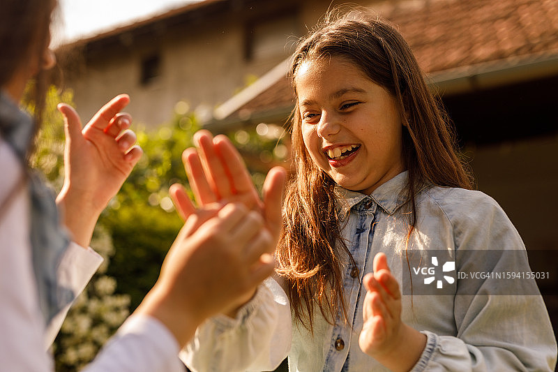 两个快乐的女孩坐在阳光明媚的花园里，玩拍手游戏图片素材
