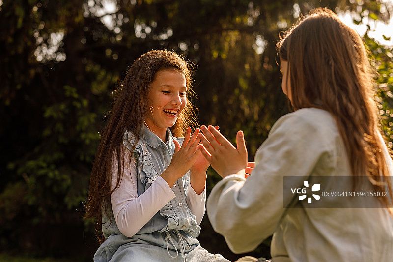 两个快乐的女孩坐在阳光明媚的花园里，玩拍手游戏图片素材