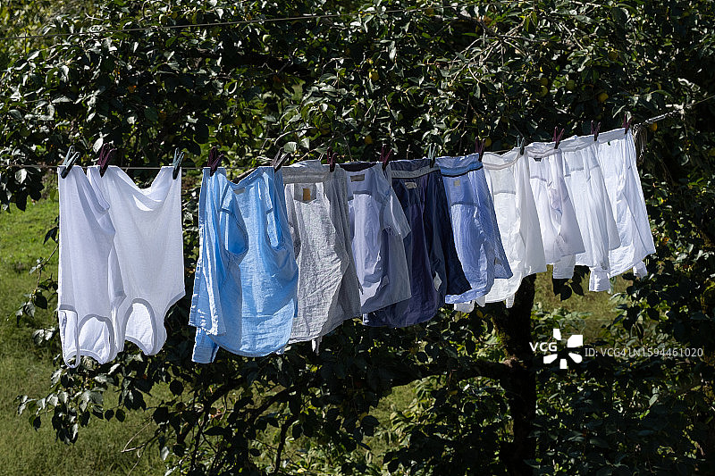 晴朗夏日，绳子上晾晒着干净的毛衣、裤子和T恤，背景是蓝天。洗过的女士、男士和儿童衣服、床上用品晾晒在晾衣绳上。家务概念图片素材