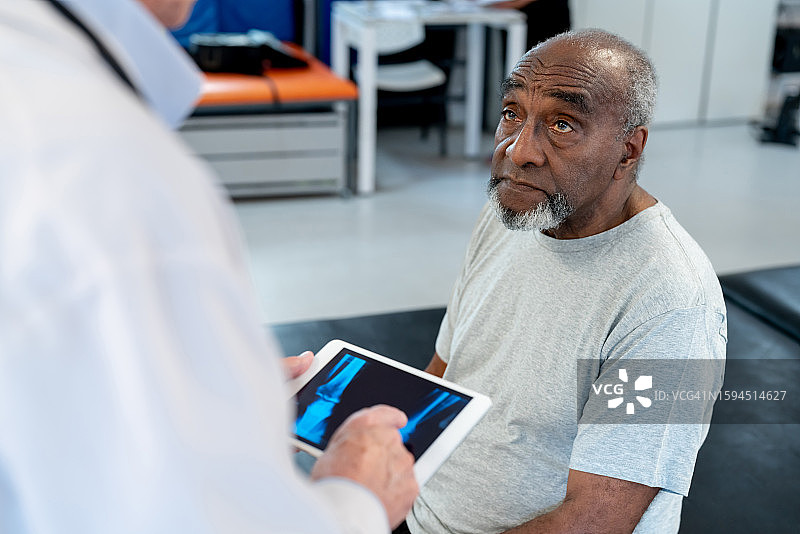 年长的黑人患者看起来很担心，而无法辨认的正骨医生正在数字平板电脑上看他的X光片图片素材