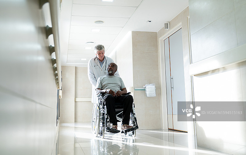 快乐的医生和坐在轮椅上的年长黑人病人交谈，并带他去医院做检查图片素材