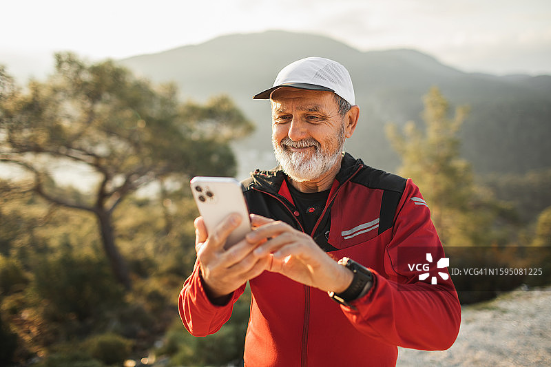 在山区美丽的地方户外跑步后，快乐地笑着的老年男人用手机进行视频通话图片素材