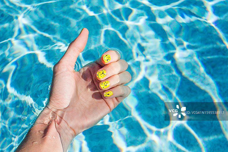 游泳池中的女人的手腕，女人的手，黄色指甲油的夏日指甲图片素材