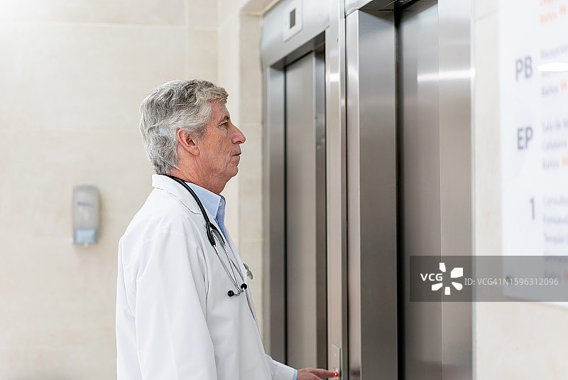 在医院等电梯的年长男医生正在按按钮图片素材