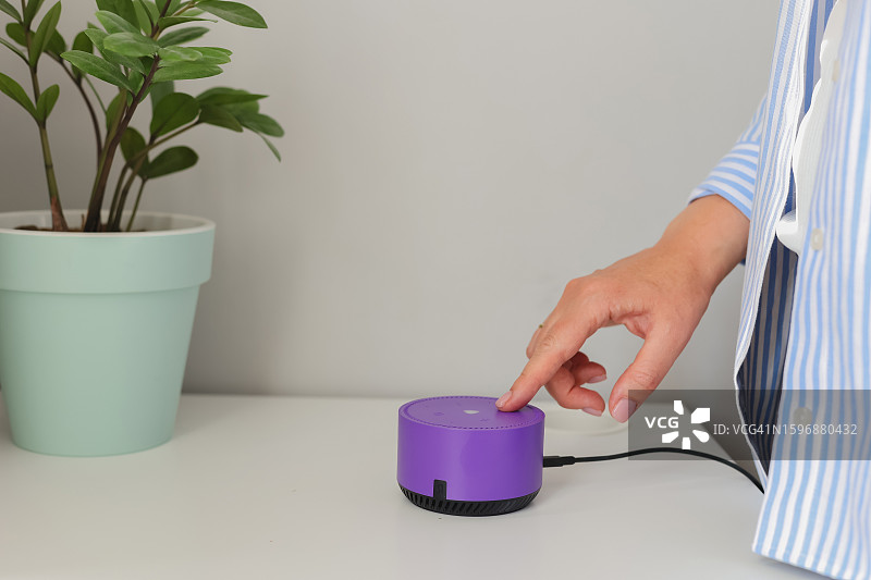 女人手触摸桌上的智能音箱，语音控制家居设备图片素材