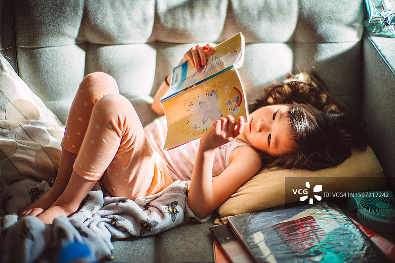 快乐的女孩在家舒适地躺在沙发上看书图片素材