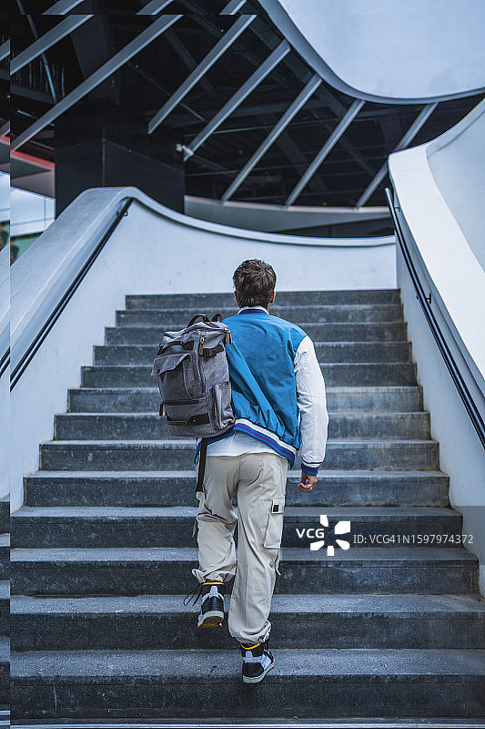 身穿蓝色夹克的年轻男子背着背包上楼梯图片素材