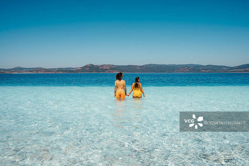 身穿鲜艳泳装的年轻夫妇在碧绿的海水中，后视图，留白图片素材