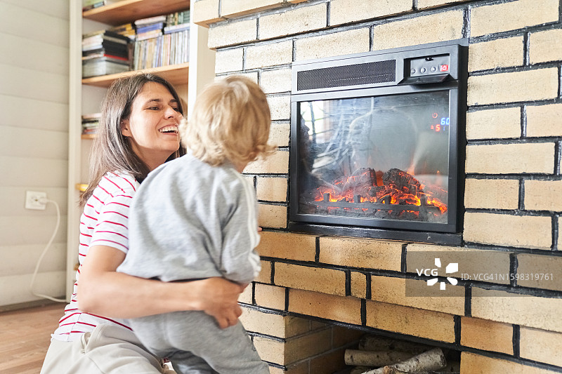 母子在壁炉旁的房子里共度时光，使用电壁炉取暖，人们很开心，生活方式照片有文案空间图片素材