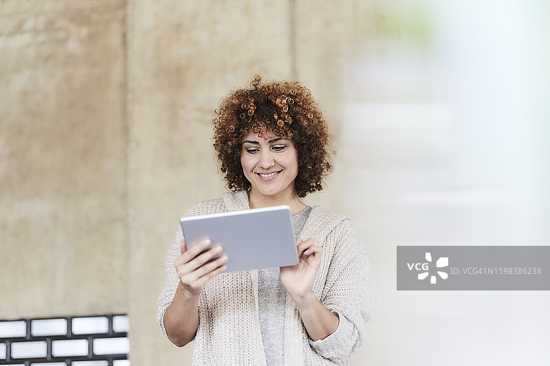 在水泥墙边使用平板电脑的微笑女性图片素材