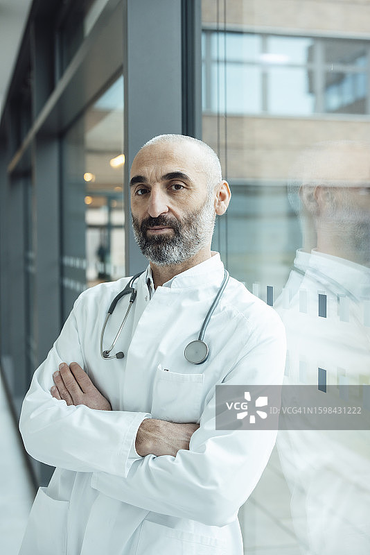 年长的医生双臂交叉靠在玻璃窗上图片素材