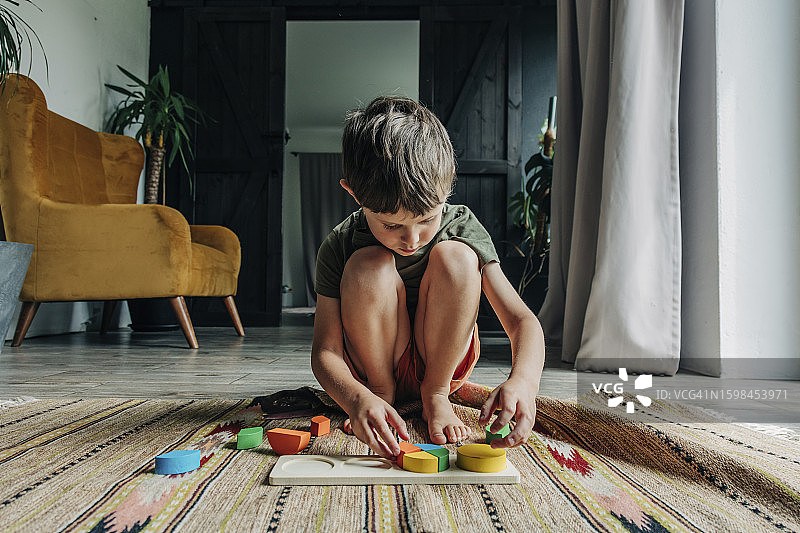 男孩在家地毯上蹲着玩积木图片素材