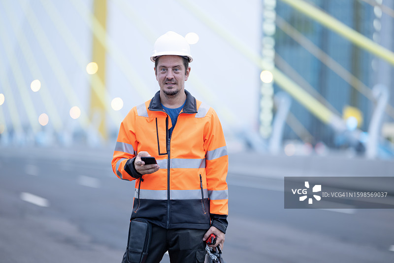 通过施工项目的项目管理软件改进规划和调度。男性项目经理在悬索桥施工现场跟踪和管理施工过程，引以为豪。图片素材