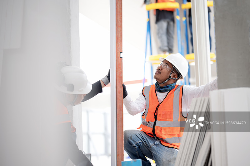 提高施工质量管理的操作质量标准设置：建筑工人根据居民楼施工现场的蓝图安装和调整门框图片素材