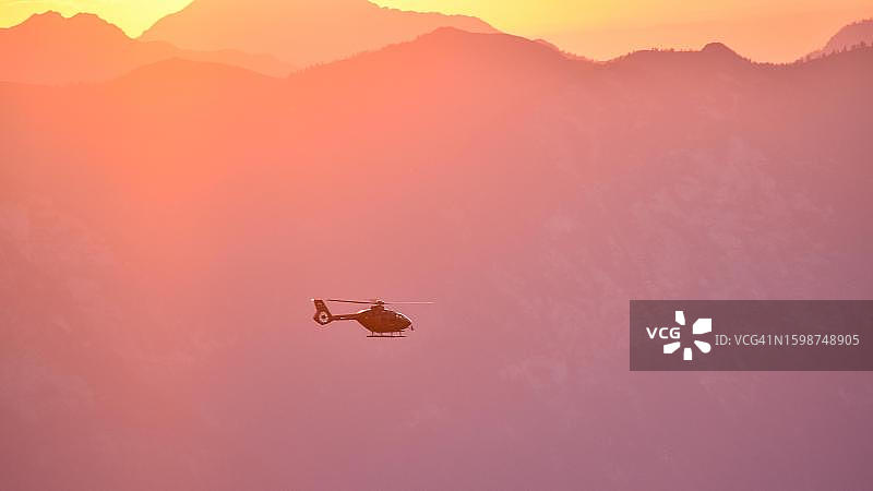 救援直升机在傍晚飞越贝希特斯加登阿尔卑斯山，德国巴伐利亚图片素材
