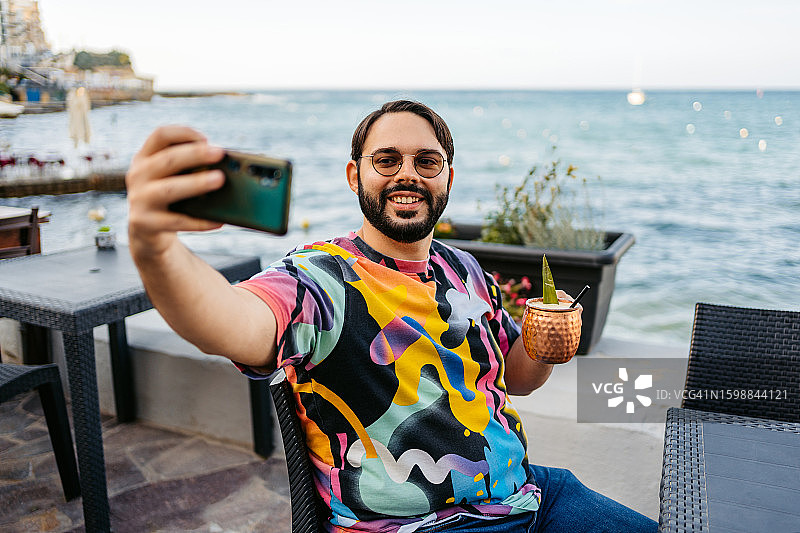 男人在马耳他海边咖啡馆自拍，手持鸡尾酒图片素材