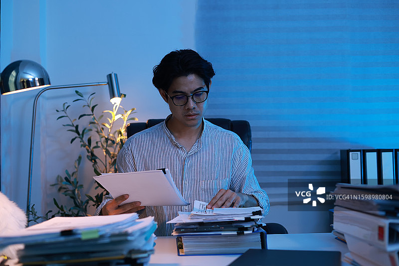 年轻商人晚上在办公室工作时查找文件图片素材
