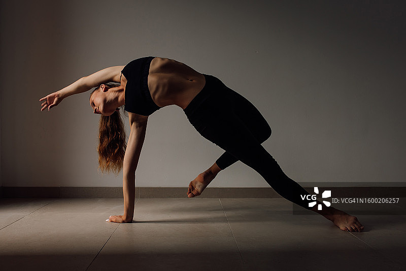 优雅年轻女子展示体操姿势，靠在一只伸出的手臂和一条腿上图片素材