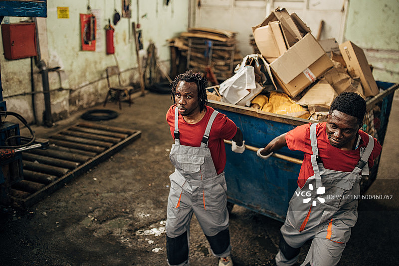 回收中心的两名工人正在移动装满纸张的大型垃圾箱图片素材