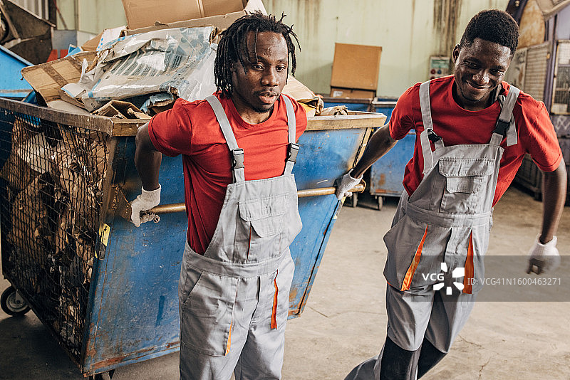 回收中心的两名工人正在移动装满纸张的大型垃圾箱图片素材