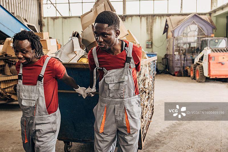 回收中心的两名工人正在移动装满纸张的大型垃圾箱图片素材