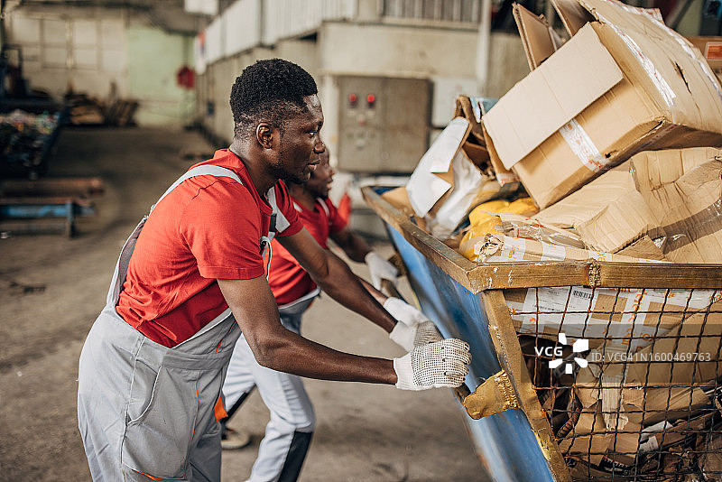 回收中心的两名工人正在移动装满纸张的大型垃圾箱图片素材