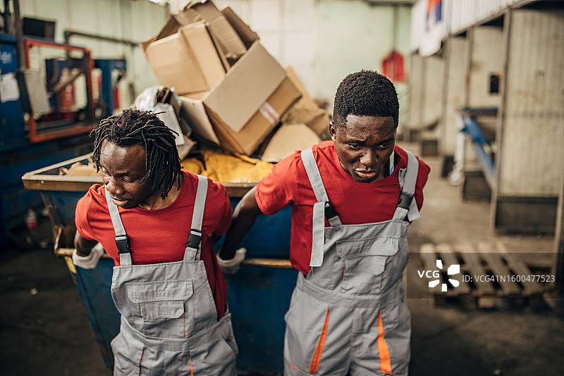 回收中心的两名工人正在移动装满纸张的大型垃圾箱图片素材