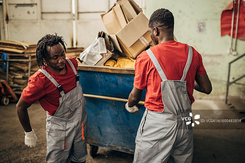 回收中心的两名工人正在移动装满纸张的大型垃圾箱图片素材