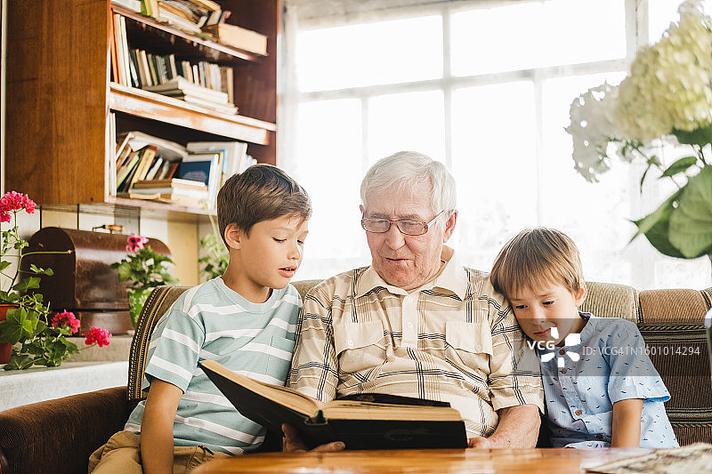 慈祥的爷爷给两个小孙子读书，温馨的家庭场景图片素材