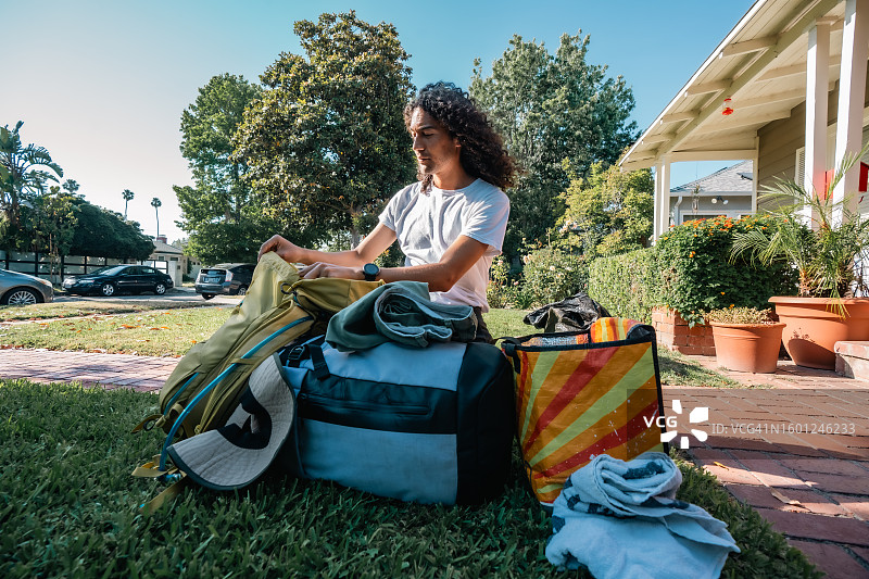 留着长卷发的年轻男子在前院打包露营包图片素材