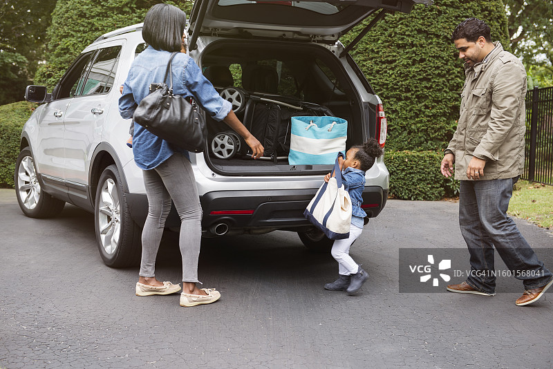 女孩在车道上提着包，家人在车旁图片素材