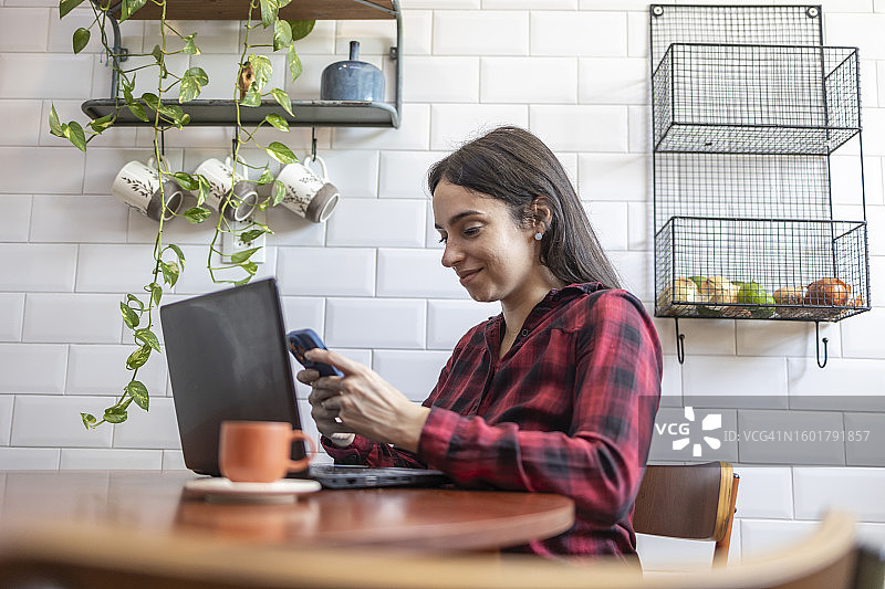 在家中厨房使用笔记本电脑和手机的白人妇女图片素材