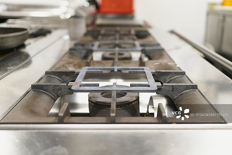 商用炉灶的燃烧器特写，背景是厨房用具图片素材