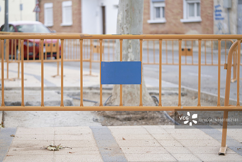 带有标志的黄色金属人行道围栏，在有树的街道上，没有人，正面视图图片素材