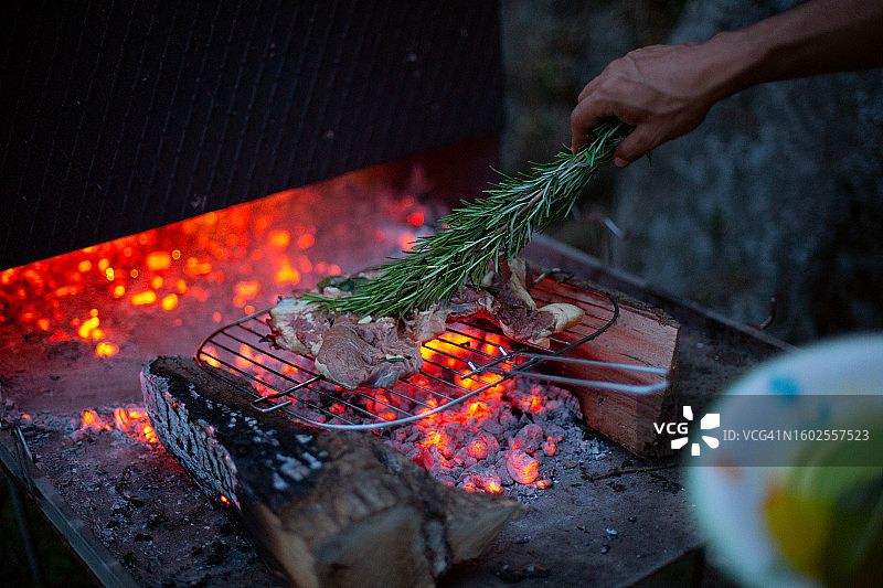 男子在烧烤架上烤肉，用迷迭香枝涂油图片素材