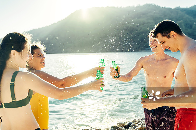 一群中年朋友在海滩上拿着饮料瓶玩得很开心，背景是海和日落图片素材