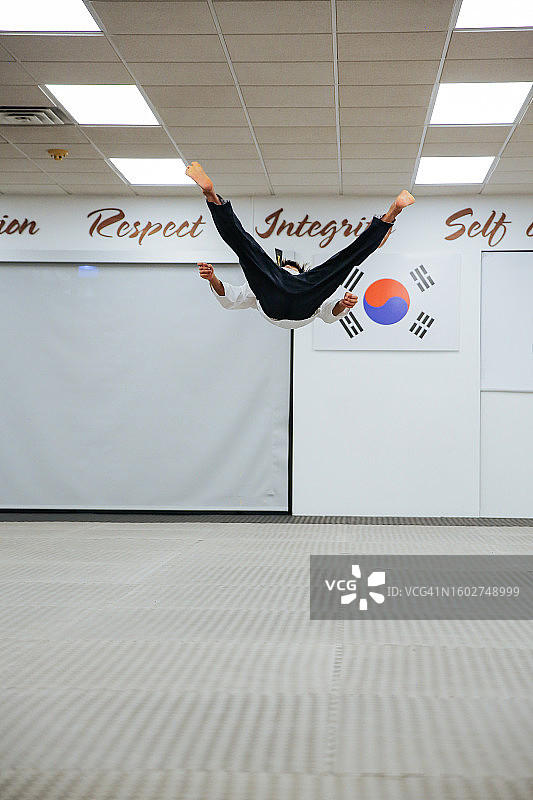 年轻男子在跆拳道品势地板动作表演中进行后空翻图片素材