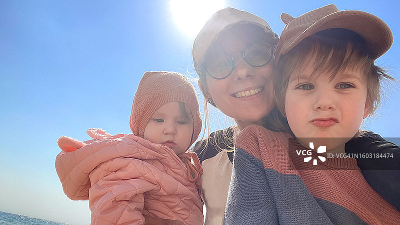 女人和儿子、女儿在海滩上用智能手机自拍图片素材