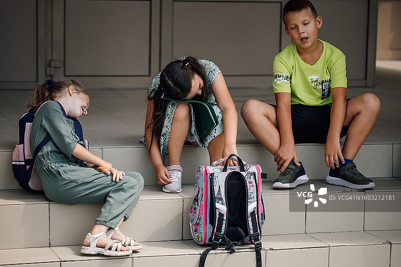 三个疲惫的学生坐在校舍楼梯上。图片素材