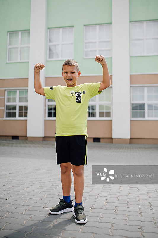 在教学楼前举起双手的金发小男孩图片素材