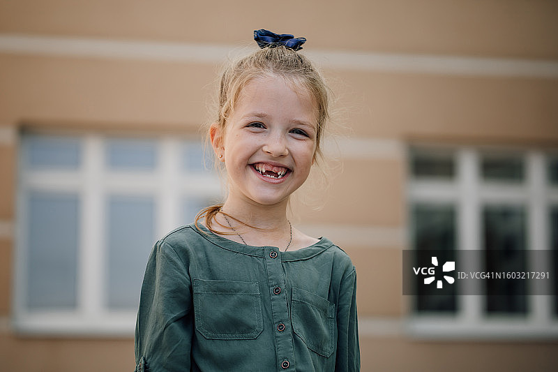 在学校大楼背景下，笑容灿烂的金发快乐女孩照片图片素材