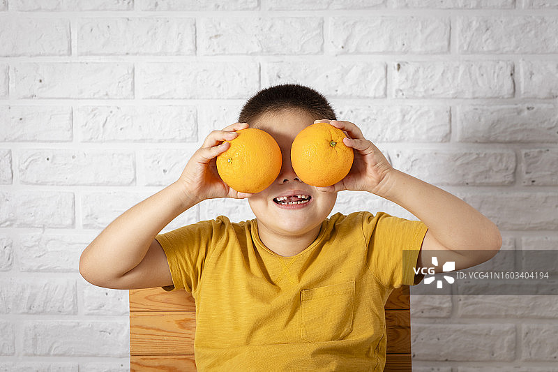 微笑的男孩靠墙拿着橙子图片素材