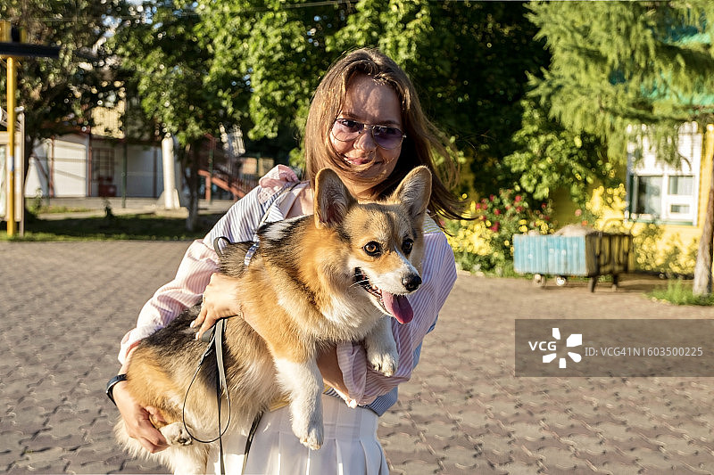 在人行道上站着彭布罗克威尔士柯基犬的微笑女性肖像图片素材