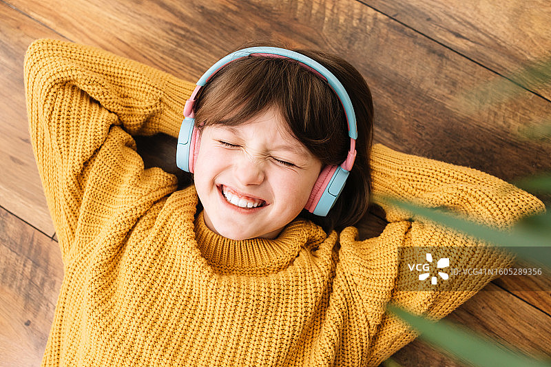 俯视角度：一个快乐微笑的少女戴着耳机听音乐，快乐的孩子图片素材