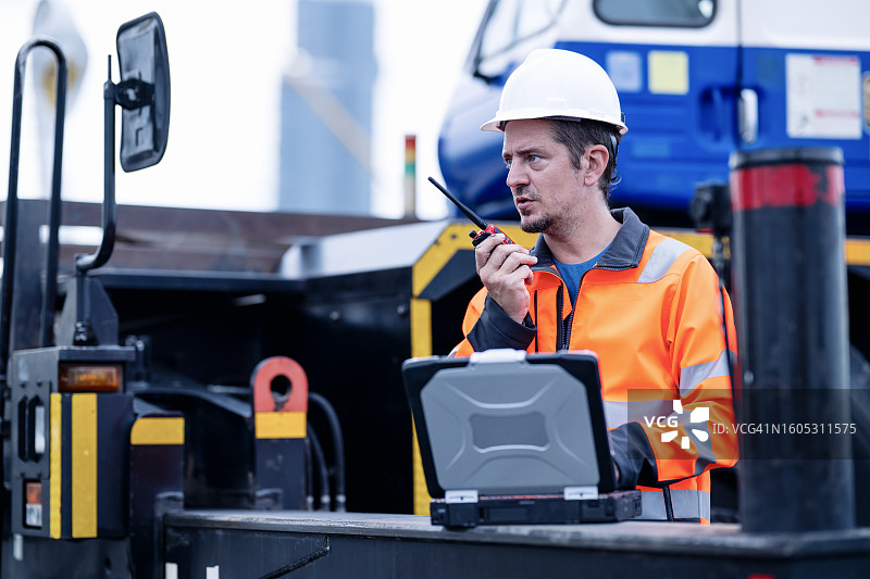 监控进度并进行调整是有效施工项目管理的关键。男性施工项目经理在现场操作，通过对讲机与团队讨论和跟进项目任务。图片素材