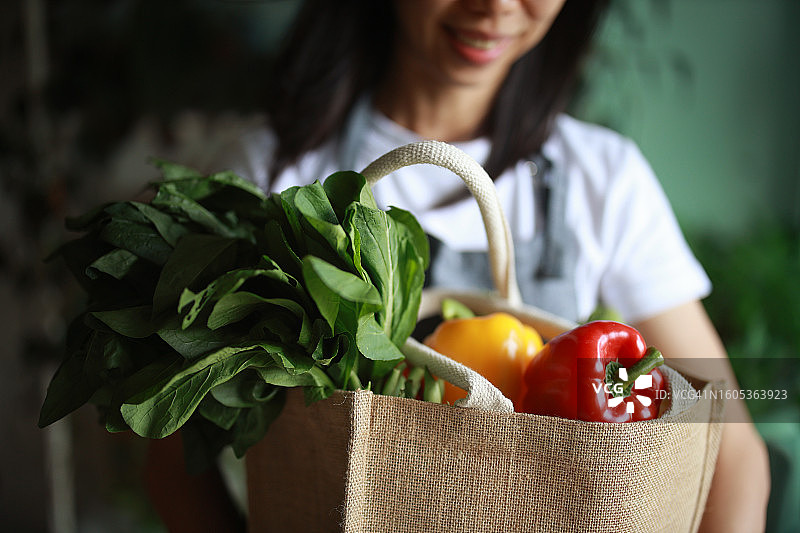 年轻的亚洲女性购买新鲜有机果蔬后，拎着可重复使用的购物袋回家，体现负责任的购物、零浪费和可持续生活方式图片素材